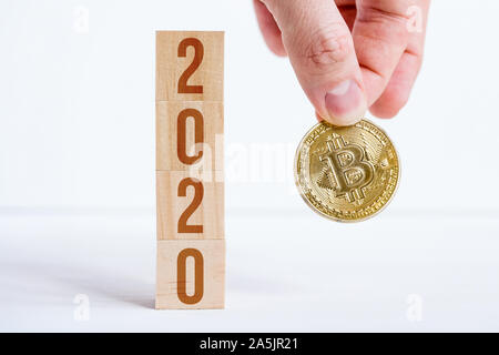 Tenir la main avec Bitcoin 2020 cubes en bois sur les numéros o avec un fond blanc. Le succès de cryptocurrency dans la nouvelle année. Close up. Banque D'Images