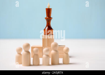 Le concept de la tête de l'entreprise fait une annonce à son personnel. King sur glaçons en face de figures en bois sur un fond bleu. Close up. Banque D'Images