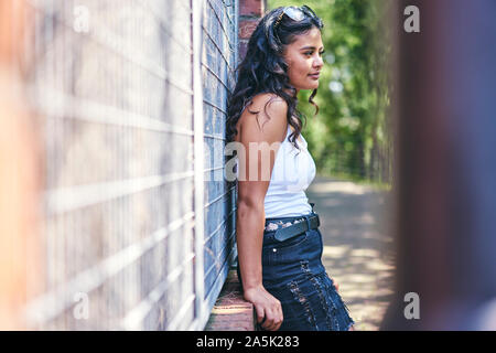 Jeune femme avec de longs cheveux noirs leaning against wall Banque D'Images