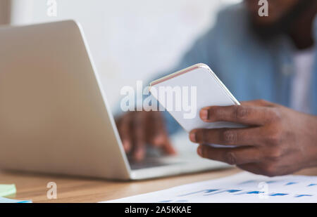 Méconnaissable african american businessman using smartphone et typing on laptop Banque D'Images