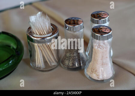 Le sucre, le sel et poivrière en verre et quelques cure-dents sur une table avec nappe beige. Image cuisine closeup couleur des détails. Banque D'Images