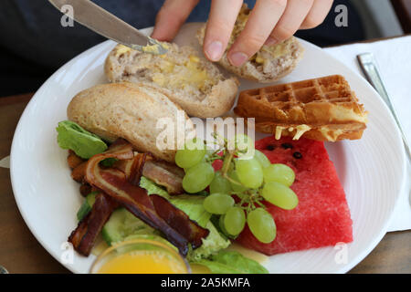 Assiette de petit-déjeuner sain articles y compris les fruits comme le melon et raisins avec du bacon, des gaufres et de sandwich rouleau. Repas idéal pour commencer une journée ! Banque D'Images