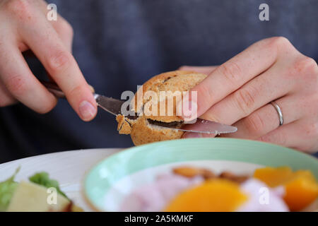 La préparation d'un petit-déjeuner délicieux et sains. Sur cette photo vous pouvez voir un gros plan d'une personne beurrer un sandwich rouleau. Yummy ! Banque D'Images