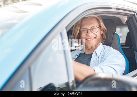 Young adult man sitting in car and smiling Banque D'Images