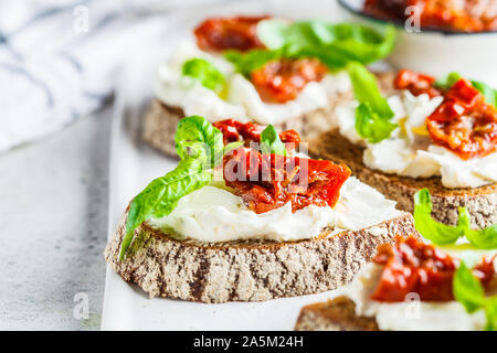 Des sandwichs avec du fromage cottage et de tomates séchées au soleil sur un tableau blanc. Banque D'Images