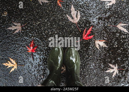 Les pieds dans des bottes en caoutchouc vert olive debout dans une flaque d'eau avec les feuilles tombées. Banque D'Images