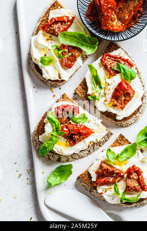 Des sandwichs avec du fromage cottage et de tomates séchées au soleil sur un tableau blanc. Banque D'Images