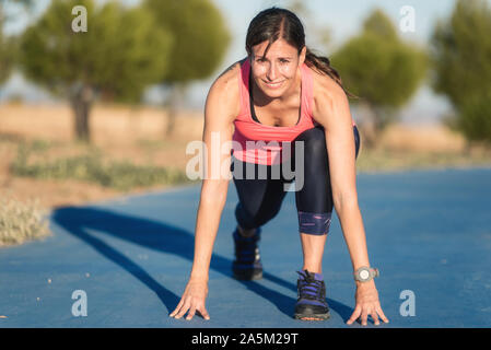 Femme athlétique sur une piste de course s'apprête à démarrer exécuter . Banque D'Images