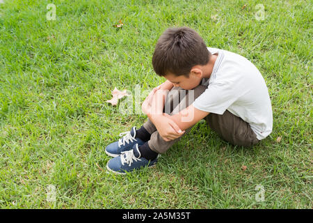 Vue latérale d'un enfant qu'à la bas assis sur l'herbe. Désemparé, la solitude et le malheur des concepts. Banque D'Images