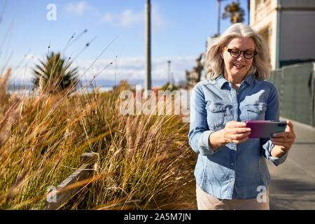 Smiling senior woman using mobile phone while standing at Manhattan Beach Banque D'Images