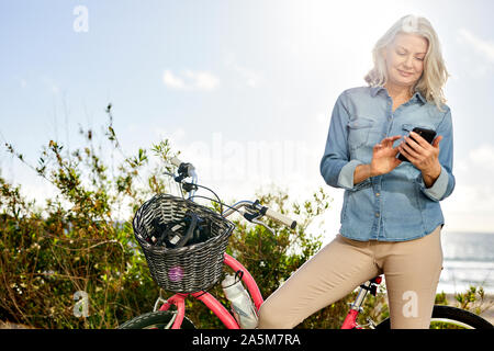 Low angle view of senior woman using mobile phone while standing en vélo contre le ciel Banque D'Images