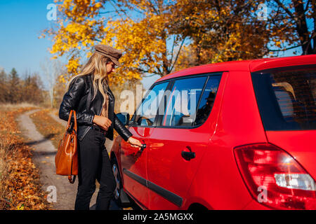 Voiture d'ouverture de porte. Femme ouvre voiture rouge avec la clé sur la route de l'automne. Serrures de porte conducteur Banque D'Images