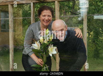 Vieux couple heureux avec des fleurs dans un verre à effet de serre près de summer house Banque D'Images