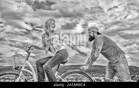 Homme pousse fille faire du vélo. Vélo fille tandis que l'homme la soutenir. Aide à croire en vous-même. Impulsion L'impression de commencer à bouger. Des promenades en vélo femme fond de ciel. Pousser et la promotion. Impulsion à se déplacer. Banque D'Images