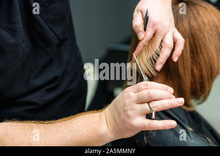 Le coiffeur ne une coupe avec des ciseaux de cheveux pour une jeune femme. Coupes de cheveux coiffeur femme close up. Banque D'Images