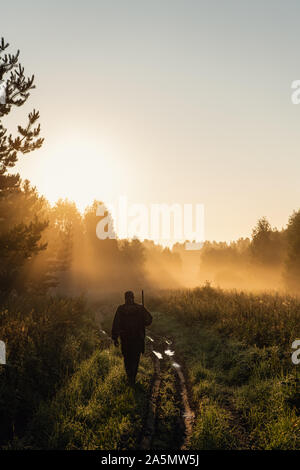 Vintage hunter marche la route forestière. Carabine Hunter qui se profile dans le magnifique coucher du soleil ou le lever du soleil. Hunter visant fusil en forêt. Banque D'Images