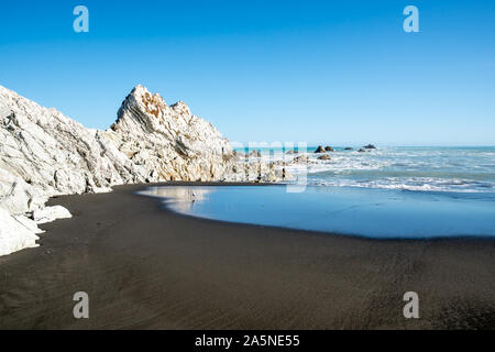 Le contraste de la plage de sable noir et le spectaculaire white rock à White Rock Beach Cape Palliser Banque D'Images