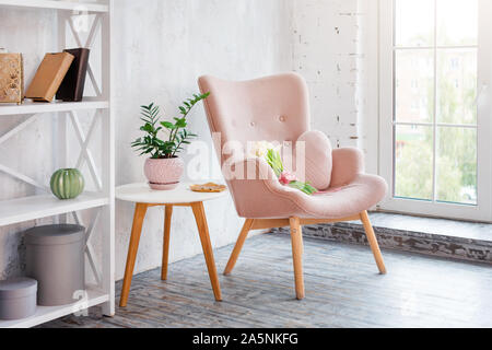 Rose élégant fauteuil avec coussin en forme de coeur dans un intérieur minimaliste. Décor en bois étagère avec près de mur gris. Bibliothèque avec des bougies Banque D'Images