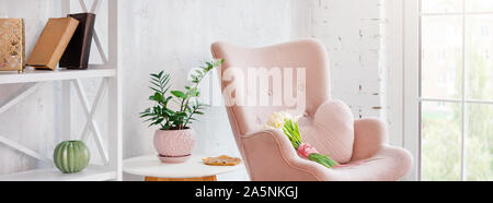 Rose élégant fauteuil avec coussin en forme de coeur dans un intérieur minimaliste. Décor en bois étagère avec près de mur gris. Bibliothèque avec des bougies Banque D'Images