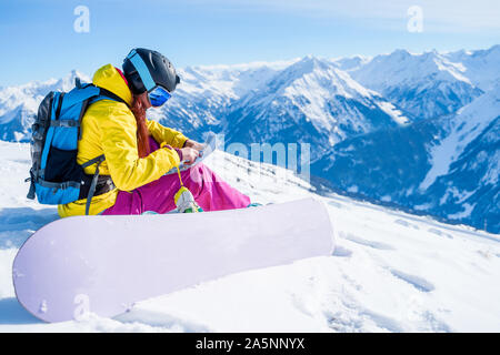 Photo de côté jeune femme sport avec la carte dans ses mains et snowboard assis sur pente enneigée en hiver Banque D'Images