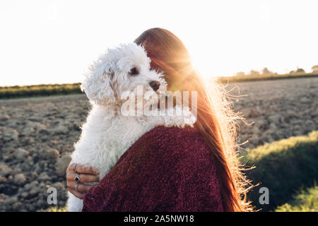 Woman hugging son chien sur le terrain au coucher du soleil Banque D'Images