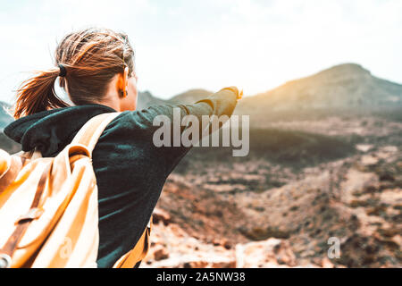 Jeune femme en randonnée sur le sommet de la montagne pointant du doigt au coucher du soleil Banque D'Images