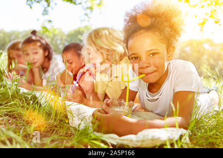 Heureux les enfants multiculturels boire de l'eau avec de la paille en été sur un pré Banque D'Images