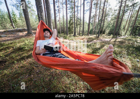 Man reading book in hammock in forest Banque D'Images