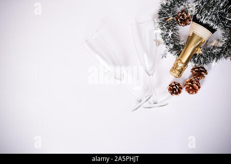 Noël ou Nouvel An composition. Concept minimaliste de champagne bouteille avec deux verres, Garland et pomme de décor sur fond blanc. Chr Banque D'Images