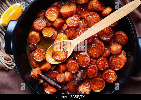 Confit d'ignames, patates douces cuites avec du jus d'orange, la cannelle, le sucre brun et le beurre dans un plat de céramique noire, vue du dessus, macro, flatlay Banque D'Images