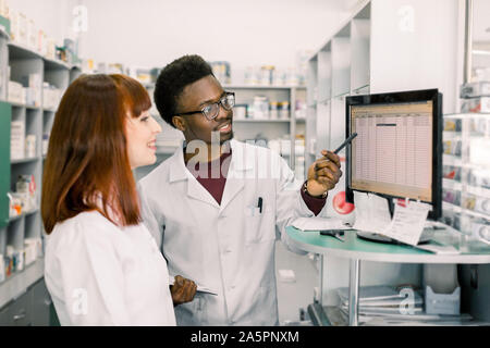 Portrait of a handsome pharmacien africain et son collègue, au comptoir d'une pharmacie, travaillant ensemble sur ordinateur. Banque D'Images