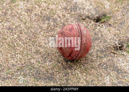 Une vue en gros plan d'un ancien puits utilisé cricket ball rouge sur une hauteur d'herbe Banque D'Images