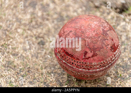 Une vue en gros plan d'un ancien puits utilisé cricket ball rouge sur une hauteur d'herbe Banque D'Images