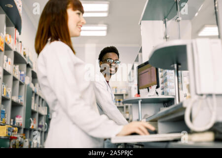 Deux pharmaciens, l'homme et la femme la vérification de l'information sur les médicaments sur l'ordinateur, pharmacie moderne Banque D'Images