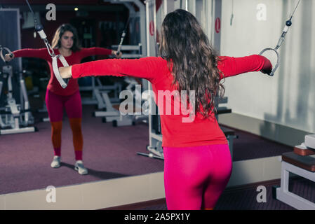 Athletic Girl engagés dans la salle de sport sur le simulateur. remise en forme sports et l'haltérophilie. femme cherche dans le reflet du miroir Banque D'Images