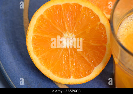 une moitié de l'orange à côté d'un verre avec du jus d'orange sur une plaque en céramique bleue Banque D'Images