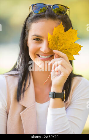 Happy woman with beautiful smile contient des feuilles d'automne jaune en face de visage Banque D'Images