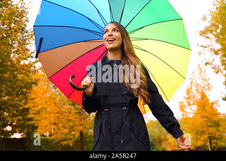 Happy girl sous parapluie arc-en-ciel. Automne woman walking in forest park enjoying outdoor avec parapluie arc-en-ciel. Banque D'Images