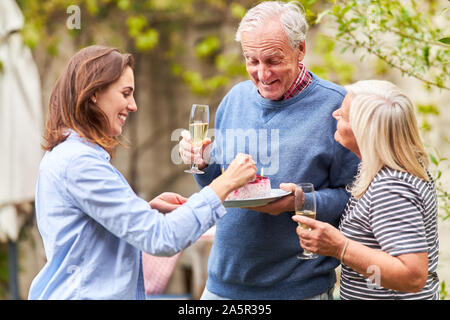 Famille célèbre l'anniversaire de grand-père avec du gâteau et du champagne dans le jardin en été Banque D'Images