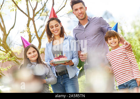 Famille avec deux enfants célébrer anniversaire avec gâteau dans le jardin en été Banque D'Images