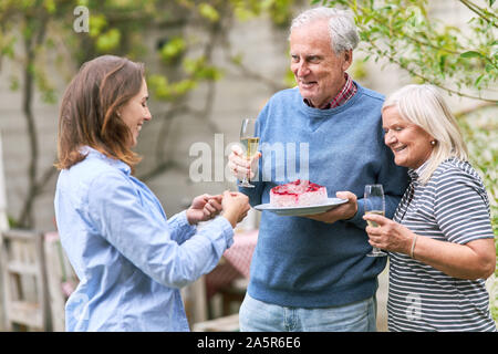 Les personnes âgées et fille célébrer anniversaire avec gâteau et champagne en été dans le jardin Banque D'Images