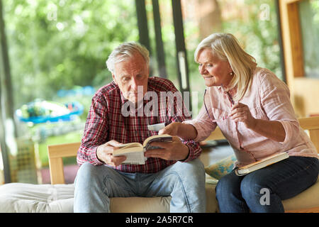 Happy senior couple lisant un livre dans le salon ou la maison de retraite Banque D'Images