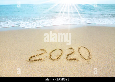 Nouvelle année 2019 sur la côte sablonneuse dans le contexte des vagues de la mer. Beau Soleil illuminent l'inscription 2020 sur le sable. Banque D'Images