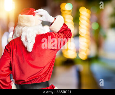 L'âge moyen bel homme portant costume père noël barbe et penser à l'arrière debout doute pointing Banque D'Images