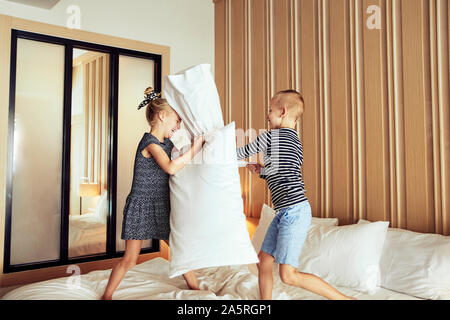 Adorable petit frère et sœur riant tout en ayant un oreiller lutte ensemble sur leur lit à la maison Banque D'Images