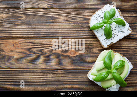 L'avocat des sandwichs avec du fromage Philadelphia, le quinoa et les feuilles de basilic. Table en bois rustique marron arrière-plan. L'espace pour le texte. Copie gratuite de l'espace. Banque D'Images