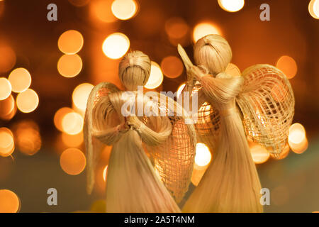 Deux anges priant de paille sur un fond de Noël floue. Beau bokeh créé par des lumières de Noël. Fait à la main traditionnelle poupée comme un tre de Noël Banque D'Images