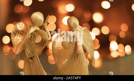 Deux anges priant de paille sur un fond de Noël floue. Beau bokeh créé par des lumières de Noël. Fait à la main traditionnelle poupée comme un tre de Noël Banque D'Images