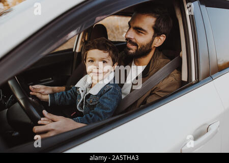 Père avec petit-fils assis sur ses genoux dans le siège du conducteur dans la voiture. Banque D'Images