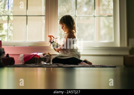 Young Girl playing dolls by window Banque D'Images